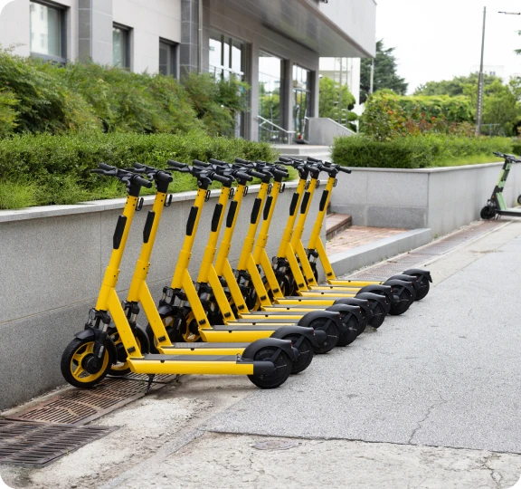 Yellow electric scooters lined up on sidewalk.